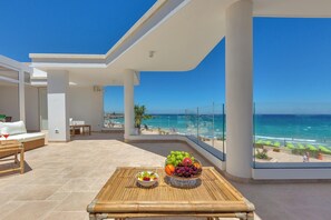 Ein Balkon mit Blick auf den Strand, ein Tisch mit Obst und ein Korbsessel.
