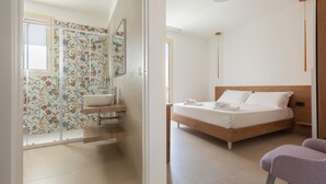 Une chambre à coucher moderne avec un lit en bois, une petite table de chevet et une salle de bain décorée d’un papier peint à motifs floraux.