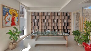 Un interior moderno con una mesa de vidrio, un cuadro abstracto grande y una pared de estantes con objetos decorativos.