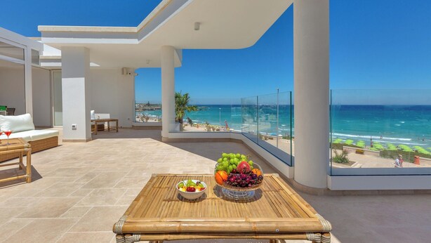 Un balcón con vista a la playa, una mesa con fruta y un sofá de mimbre.