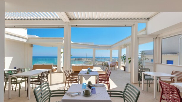 Un espacio exterior para comer con mesas y sillas, una pérgola y vistas al mar.