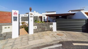 A modern building with a stone wall entrance, a wooden door, and a metal gate. - Villa Arisen by Villa Plus (Playa Blanca)