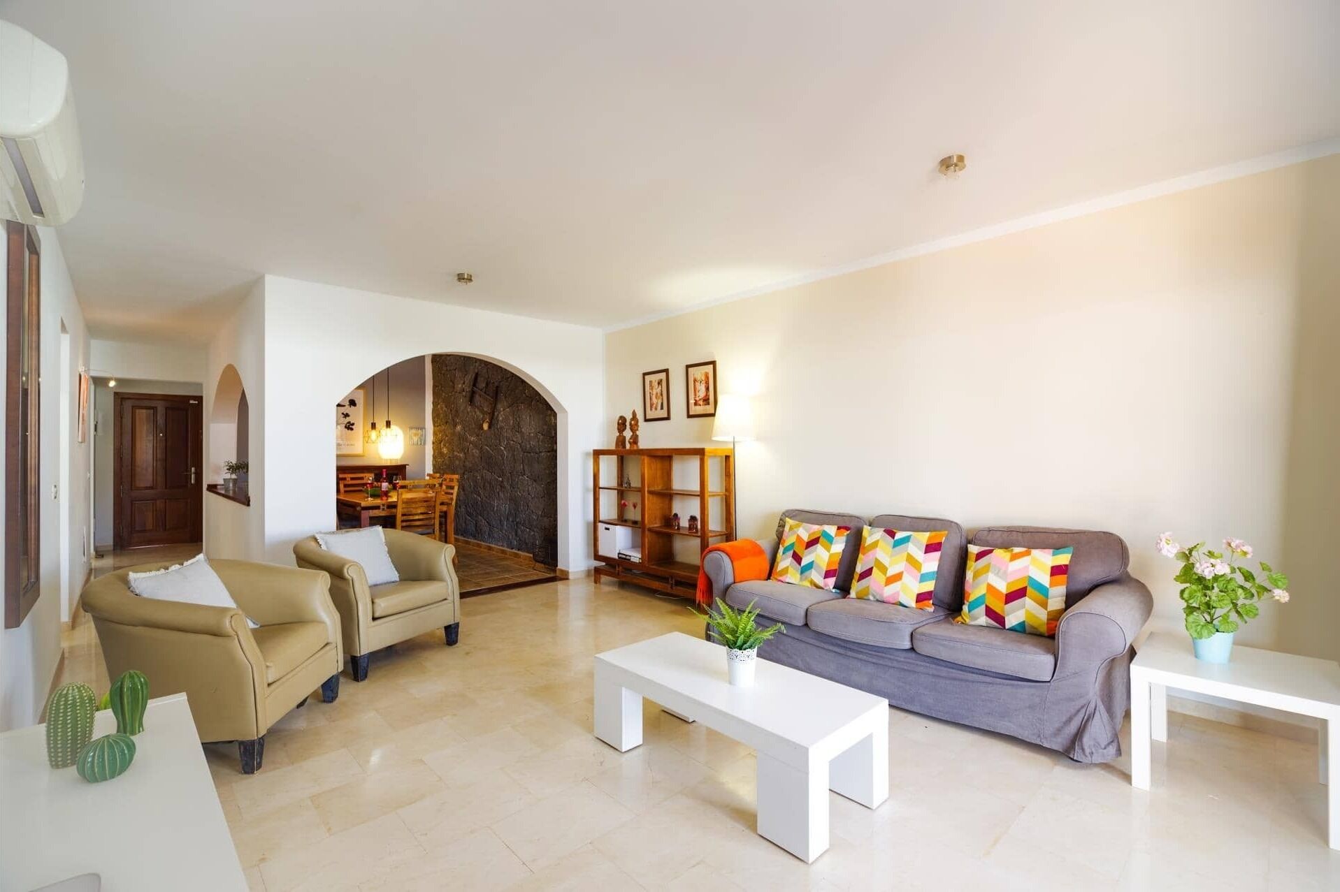 A spacious living room with a sofa, armchairs, and a coffee table. There is a dining area with a table and chairs in the background.