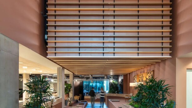 Un vestíbulo espacioso con diseño moderno, que cuenta con un pasillo central flanqueado por listones de madera y macetas de ladrillo con plantas.