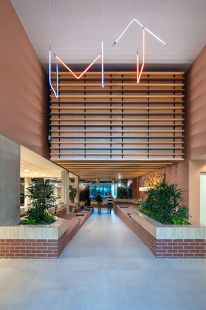 A spacious lobby with a modern design, featuring a central walkway flanked by wooden slats and brick planters with greenery.
