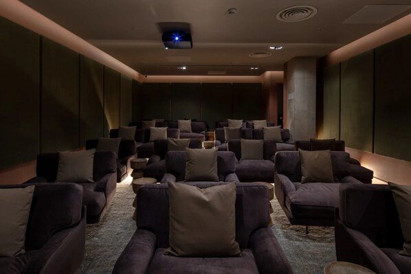 A home theater with rows of dark-colored sofas and a large screen at the front.