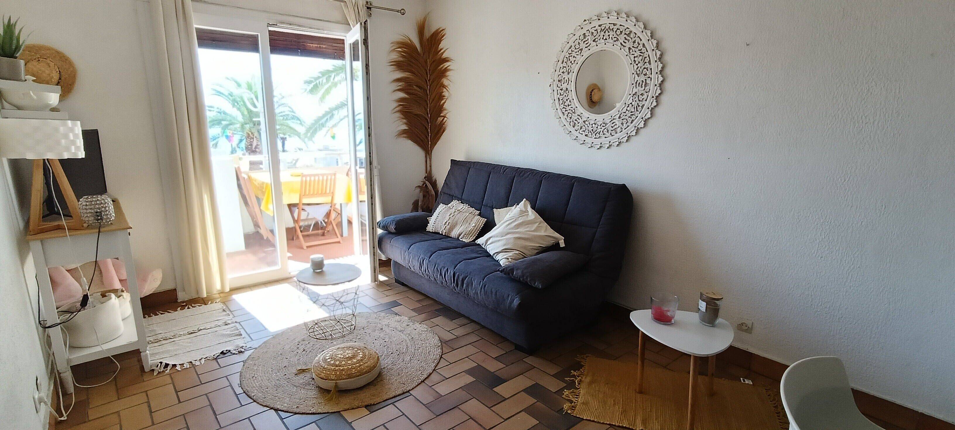 A living room with a dark blue sofa, a white round mirror, and a small round table with a candle.