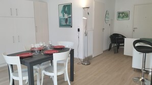 A dining area with a table set for four, white chairs, and a black tablecloth. There is a floor lamp and a radiator in the background.