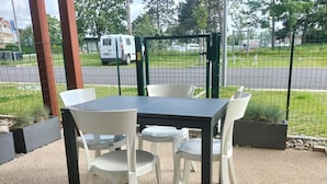 An outdoor patio with a table and chairs, surrounded by a wire fence and greenery.