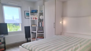 A bedroom with a bed, a bookshelf, a radiator, a window, and a desk with a computer.