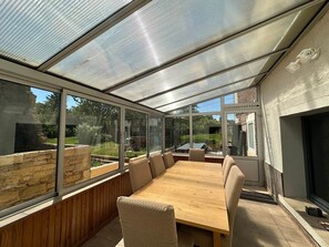 A sunroom with a large table and chairs, a stone wall, and a view of the outside. - Gîte OPLM 4* - 8 p. Near Charleville (Prix-lès-Mézières)
