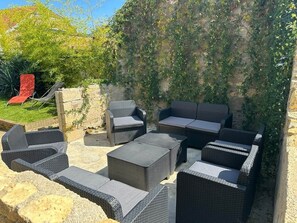 Un espace extérieur aménagé avec des meubles en osier, un mur en pierre et une chaise rouge.