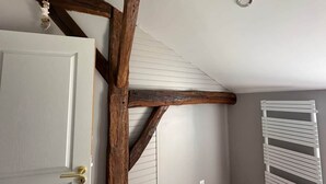 Una habitación con vigas de madera a la vista, una puerta blanca con manija de latón y un radiador blanco.