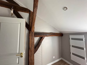 Une pièce avec des poutres apparentes, une porte blanche dotée d’une poignée en laiton et un radiateur blanc.