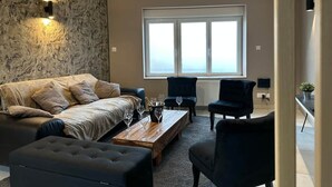 Una sala de estar con un sofá, una mesa de centro y dos sillas. Hay un ventanal con vistas.