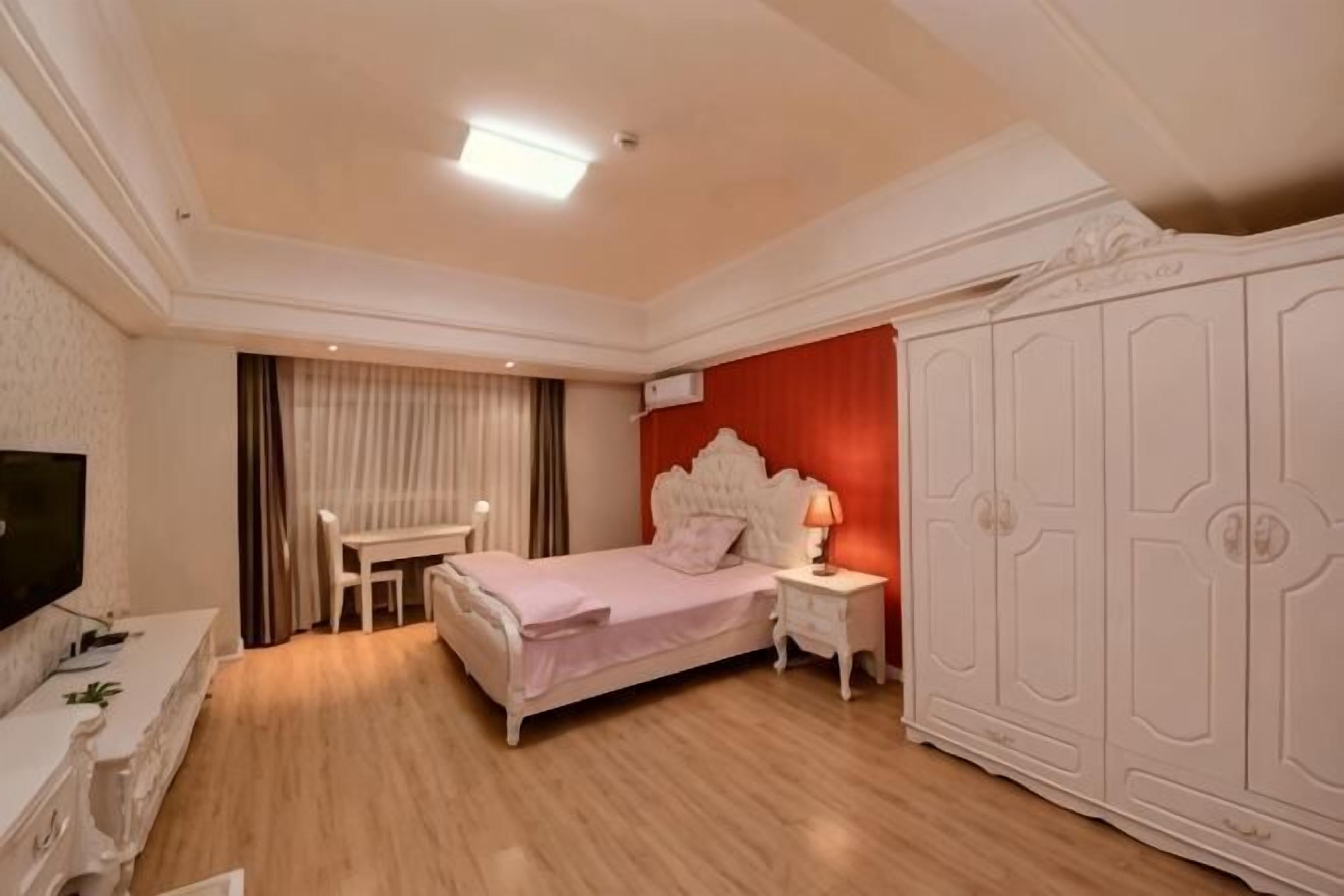 Un dormitorio con cama, mesita de noche, televisor, armario y un escritorio con silla.