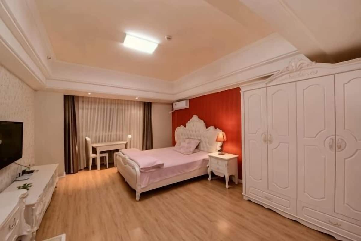 Un dormitorio con cama, mesita de noche, televisor, armario y un escritorio con silla.