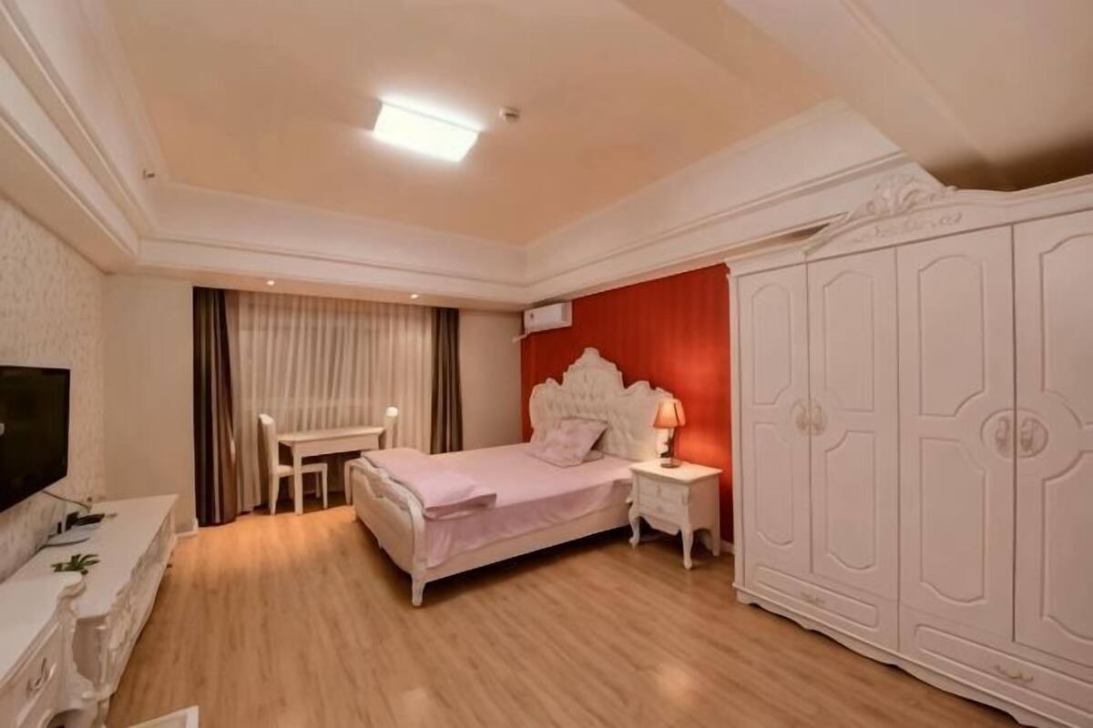 A bedroom with a bed, bedside table, TV, wardrobe, and a desk with a chair.