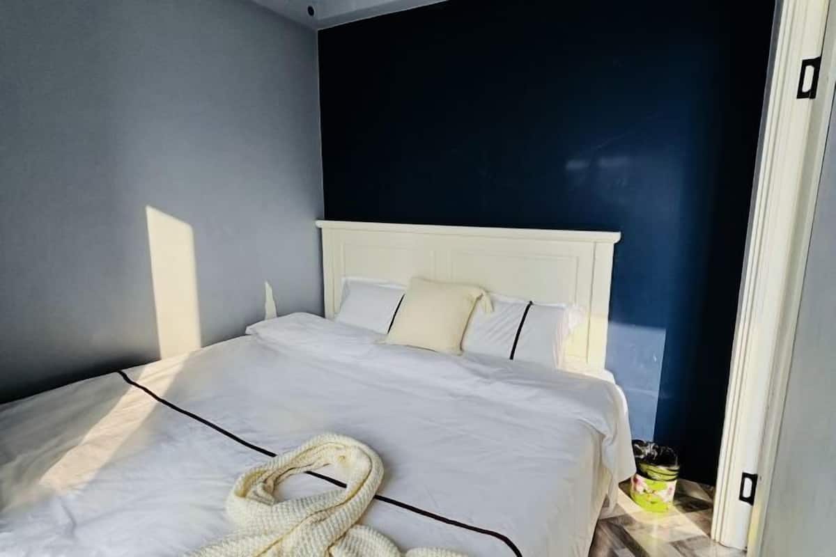 Una habitación de hotel con una cama blanca, una pared oscura y una puerta.