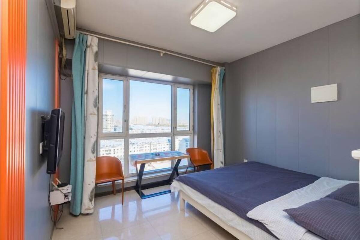 Una habitación de hotel con cama, televisión, una mesa con sillas y ventana con cortinas.