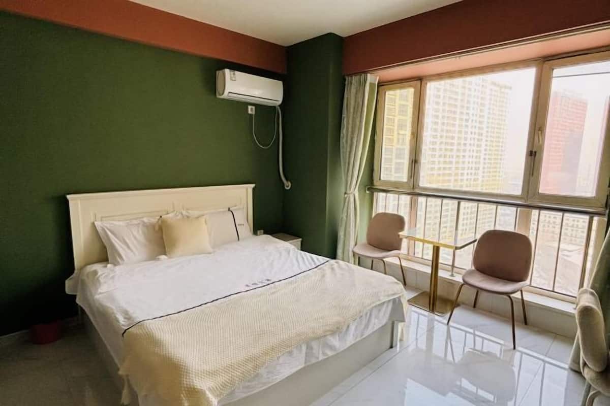 Habitación de hotel con cama, dos sillas, una mesita y ventana con vistas a edificios.