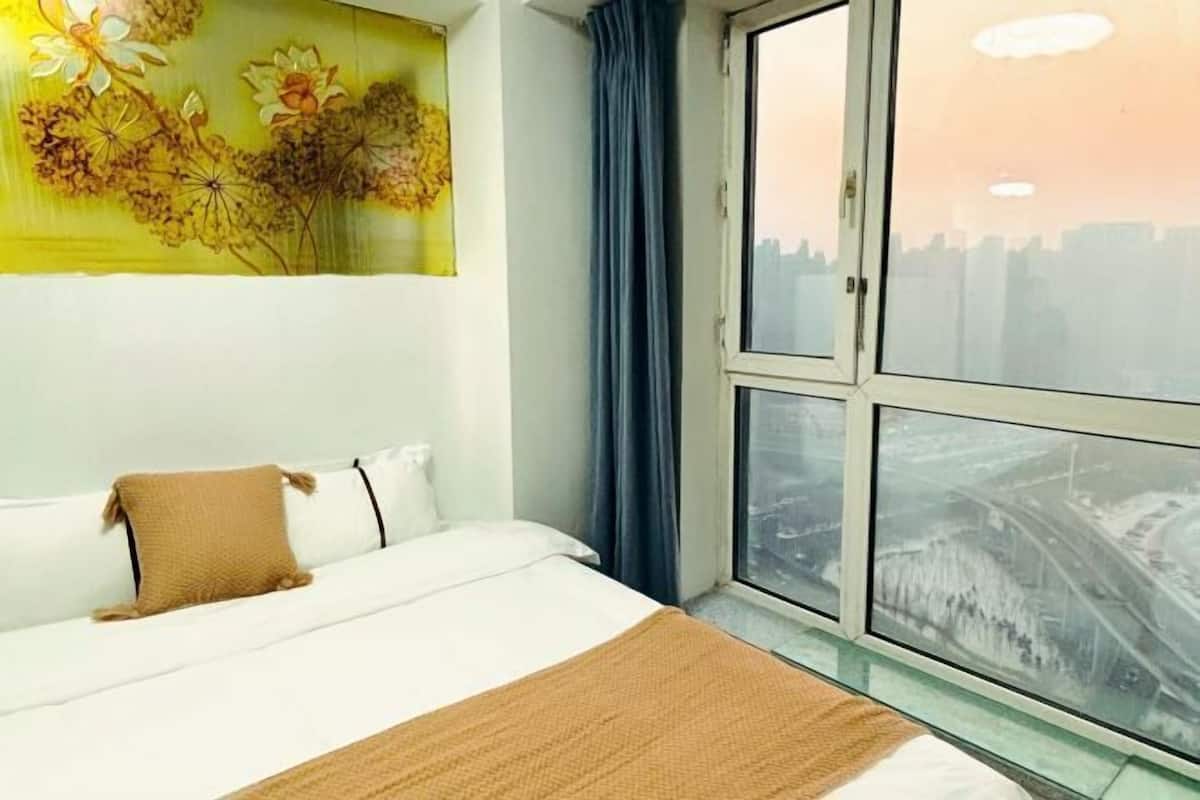 Habitación de hotel con una cama, una ventana que ofrece vista a la ciudad, una pared con un mural floral y una cortina azul.