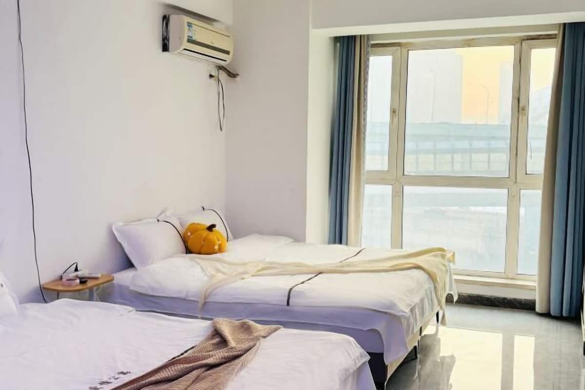 Habitación de hotel con dos camas, una ventana con cortinas y un equipo de aire acondicionado en la pared.