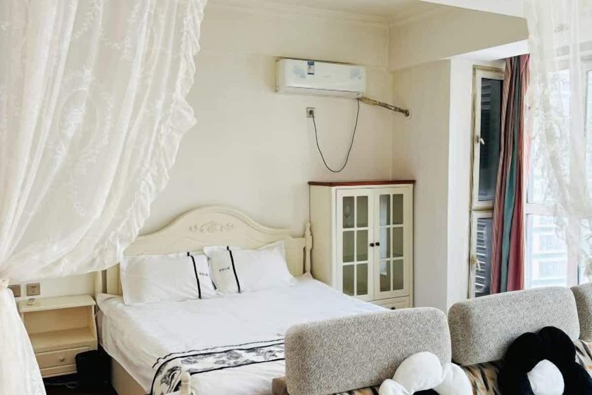 Un dormitorio con cama, mesita de noche, armario y ventana con cortinas.