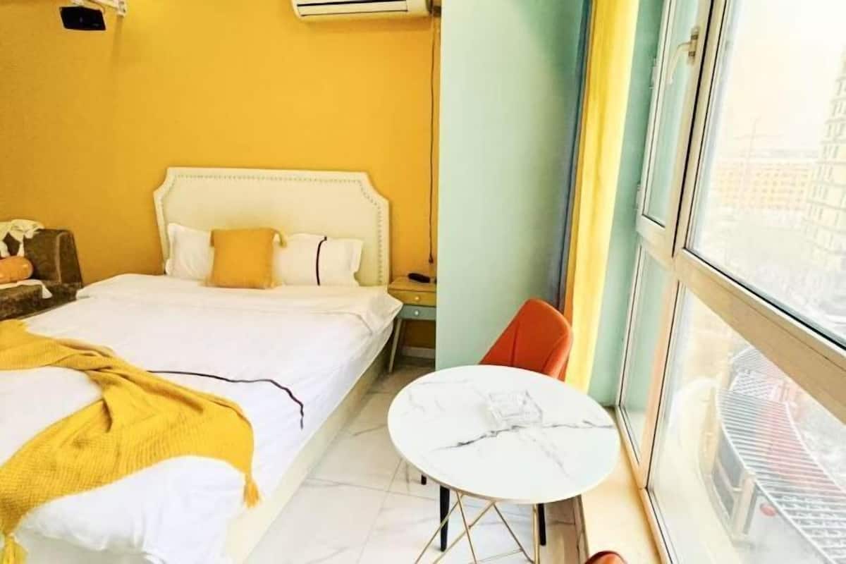 Habitación de hotel con cama, una mesita redonda y ventana con vista a edificios.