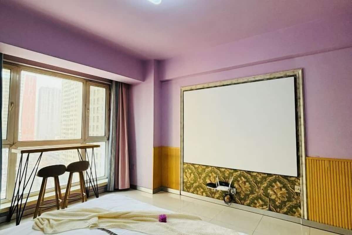 Una habitación con un ventanal grande, una cama, dos sillas y una pizarra en la pared.