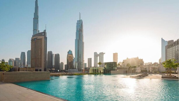 Un paysage urbain avec une tour imposante et une étendue d’eau dans laquelle se reflètent les bâtiments.