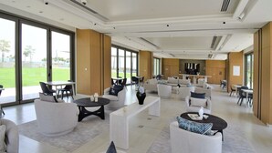 Un espace salon spacieux et moderne, doté de nombreux sièges, de grandes fenêtres offrant une vue sur l’extérieur et d’un aménagement épuré et minimaliste.