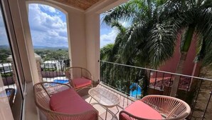 A balcony with wicker furniture and a view of a swimming pool and palm trees. - Serenity Oasis in Playa Langosta (Playa Langosta)