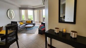 A modern living room with a sofa, chairs, a coffee table, and a dining area with a table and chairs. There is a large mirror on the wall and a window providing natural light. - Serenity Oasis in Playa Langosta (Playa Langosta)