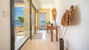 A hallway with a view to the outside, a door leading to a balcony, and a table with a vase of dried flowers. - Private Luxurious Beachfront Villa with Chef, Household Staff, Concierge  (Potrero)