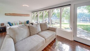 Amplia sala de estar con un sofá beige grande, una mesa de centro de madera y un televisor. La habitación tiene ventanas amplias que ofrecen vista a un patio trasero con muebles de exterior.