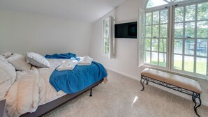 Un dormitorio con cama, una banca, televisor montado en la pared y un ventanal con vistas al exterior.
