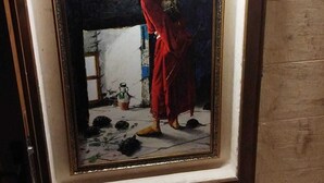 A framed artwork depicting a person in a red garment, with a tiled floor and a small plant in the background. - Ruken Hanım Konağı (Gaziantep)