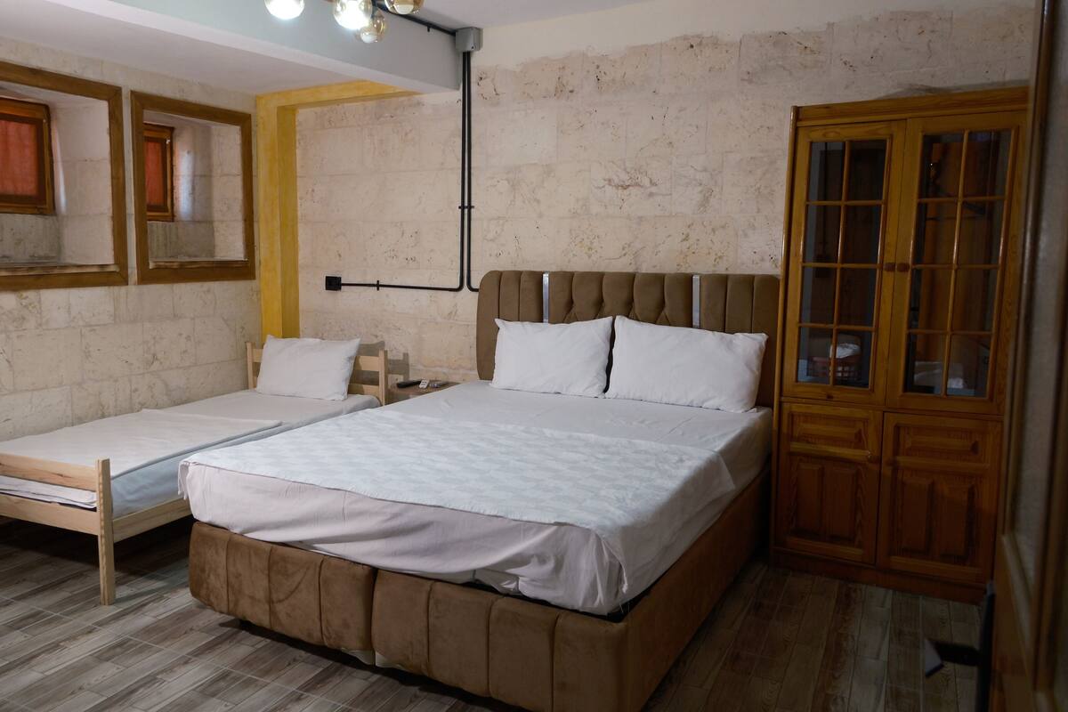 A room with two single beds and one double bed, wooden flooring, a brick wall, and a wooden wardrobe.