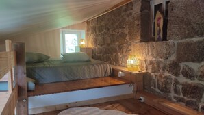 Un dormitorio abrigado en el ático, con cama de madera, paredes de piedra y una pequeña mesa con lámpara.