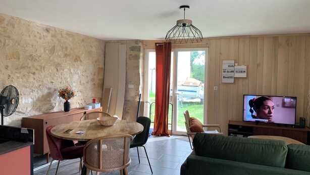 A living room with a wooden dining table, a green sofa, and a television. - Gite Indépendant 4-6 Personnes Avec Piscine Privative (Gourdon)