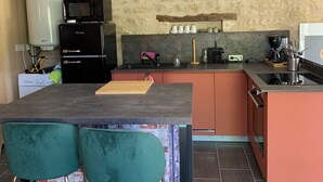 A compact kitchen with a stone wall, a built-in microwave, a coffee machine, and a small bar area with stools. - Gite Indépendant 4-6 Personnes Avec Piscine Privative (Gourdon)