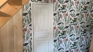 A room with a white door, wooden ceiling beams, and a wall with a bird and plant wallpaper. - Gite Indépendant 4-6 Personnes Avec Piscine Privative (Gourdon)
