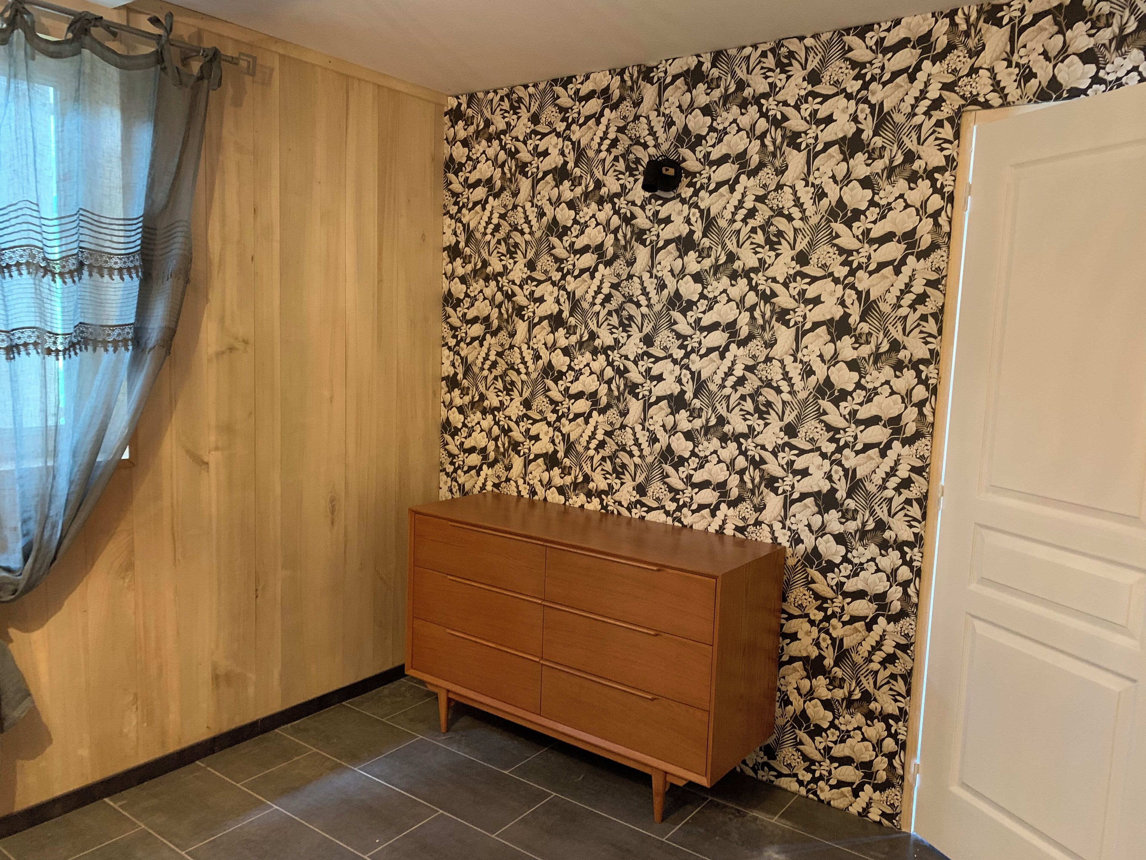 A room with a wooden wardrobe, a floral wallpaper, and a white door.