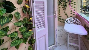 An open door leading to a balcony with a white chair, surrounded by lush green and yellow plants, and a pink neon light. - Future Hostel (Cairo)