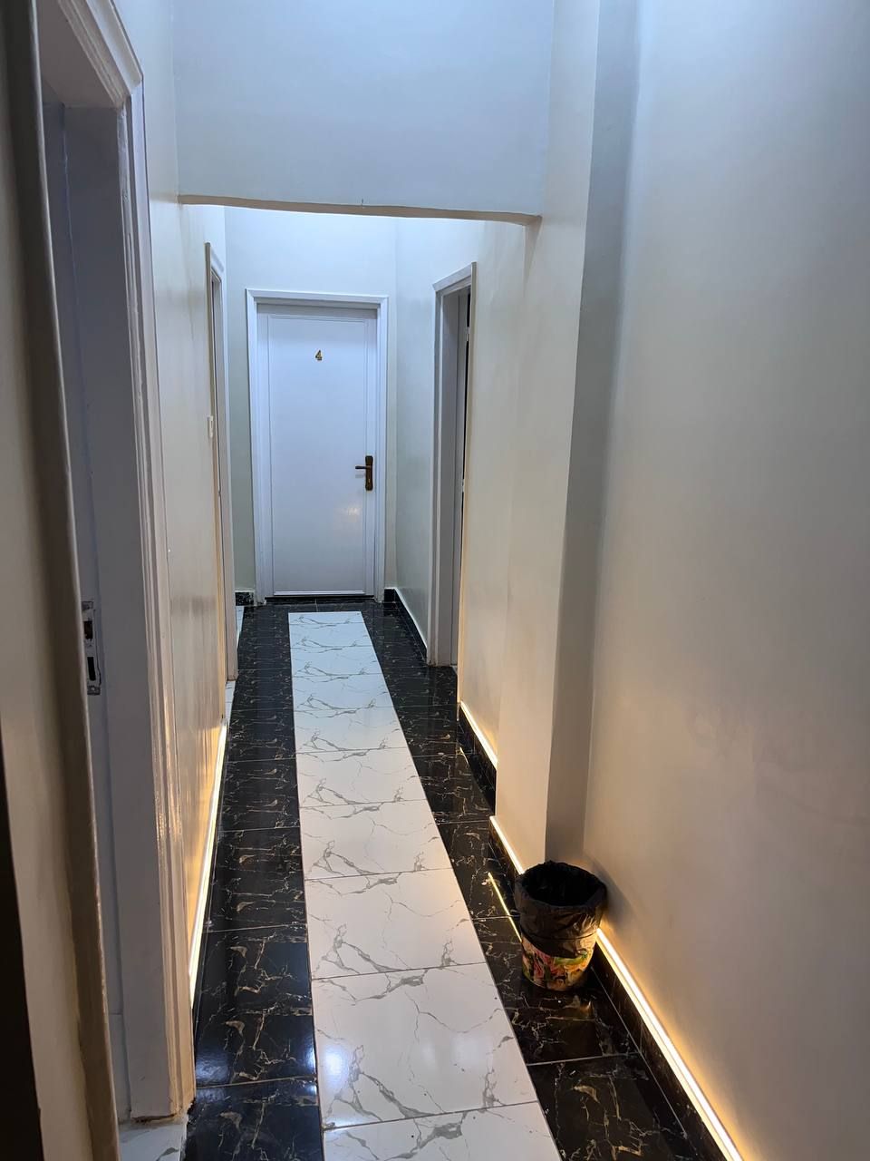 Un passadís amb terra de marbre, parets blanques i una porta al final.