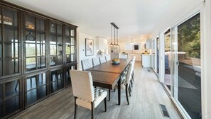 Enjoy meals in this dining area with a long table and comfortable chairs, surrounded by a large window offering a view of the outdoors.