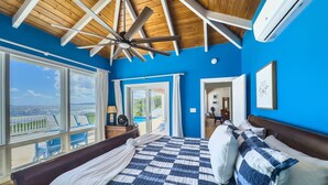 A bedroom with a large bed, a ceiling fan, and a view of the outdoors. - Toes in the Sand | Beachfront Home & Private Pool (Christiansted)