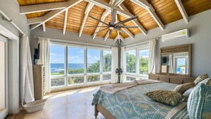 A bedroom with a large bed, a ceiling fan, and a view of the ocean. - Toes in the Sand | Beachfront Home & Private Pool (Christiansted)