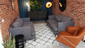 Un salón moderno con paredes de ladrillo, una pared de acento azul, un sofá oscuro, un sillón de cuero marrón y una alfombra estampada.